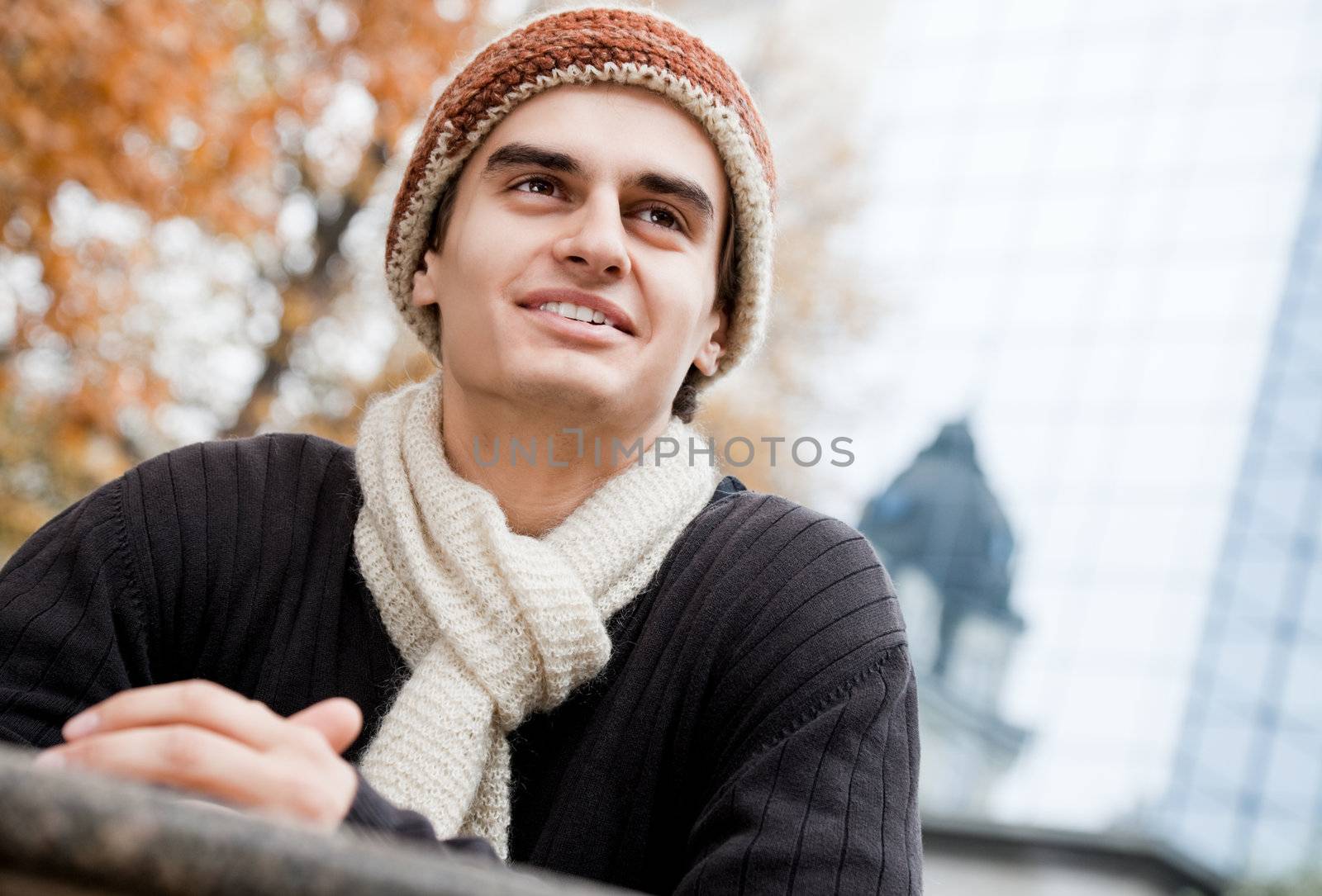 Portrait of happy male wearing shawl and hat smiling in park on autumn day