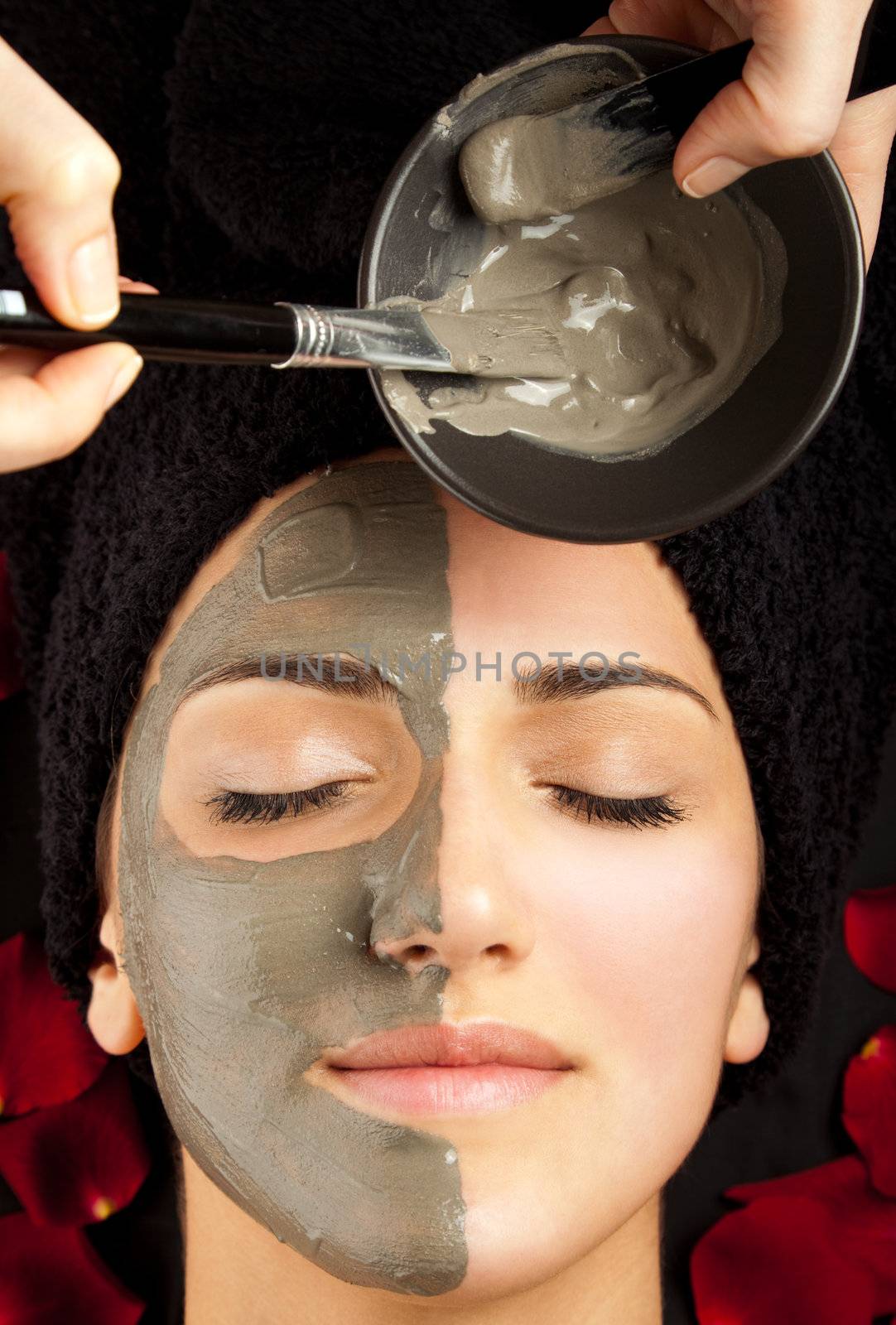 applying clay mask on young woman's face, half covered