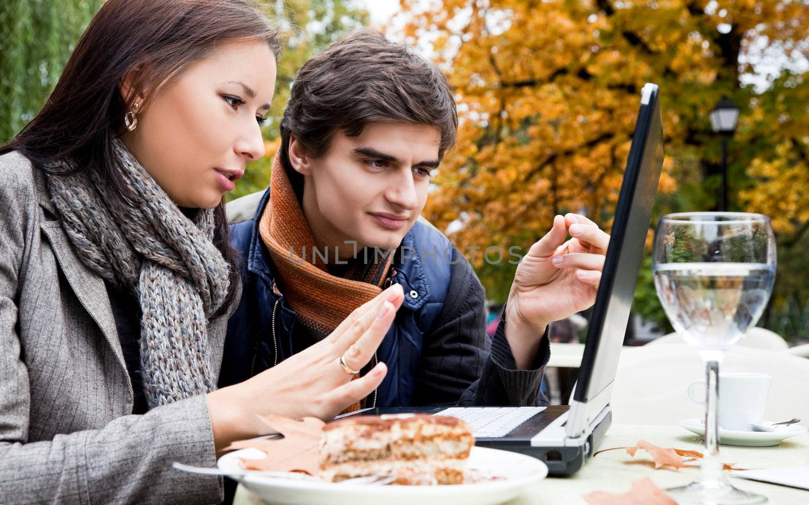 Young couple sitting nad talking behind laptop in autumn park