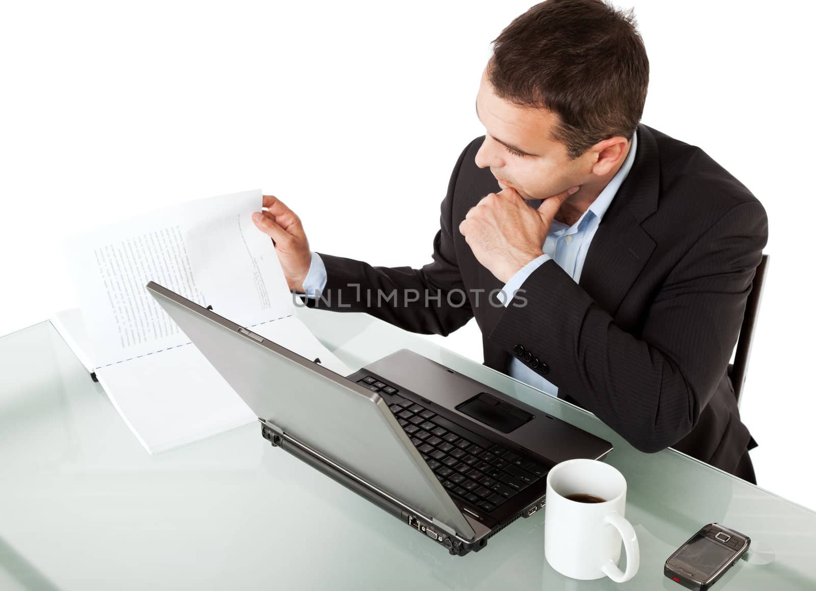 Businessman reading documents on his desk behind laptop with cup of coffee and cellular