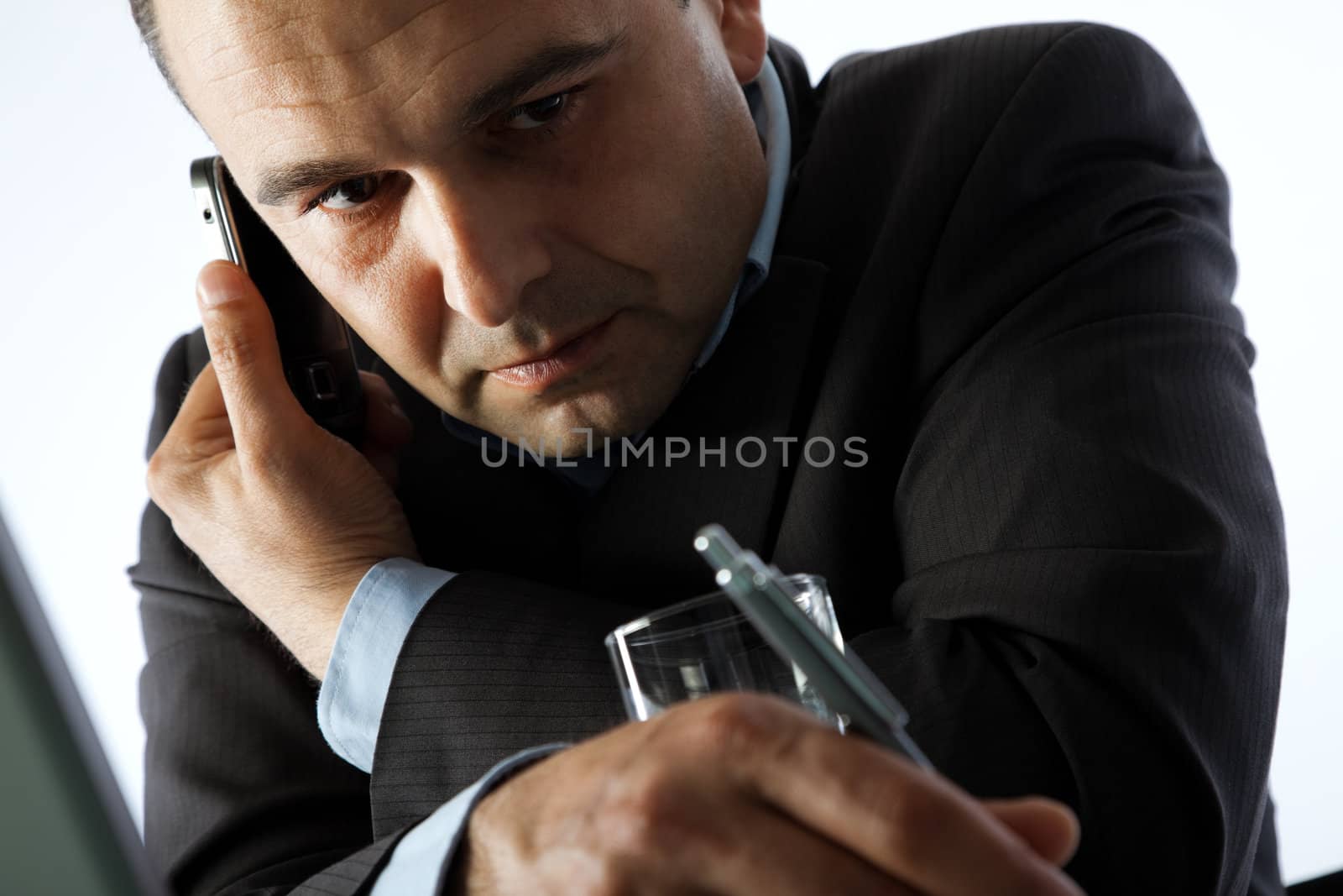 Portrait of businessman busy on the cell phone, writing down with pen