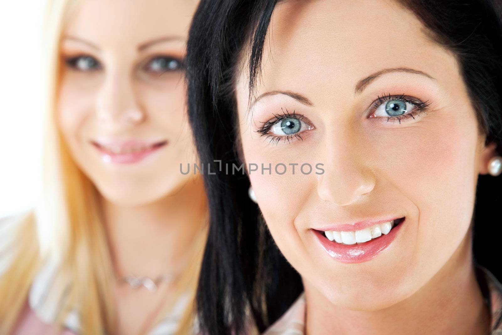 Close-up of two beautiful women smiling and looking at camera, focus on brunette, blonde in back