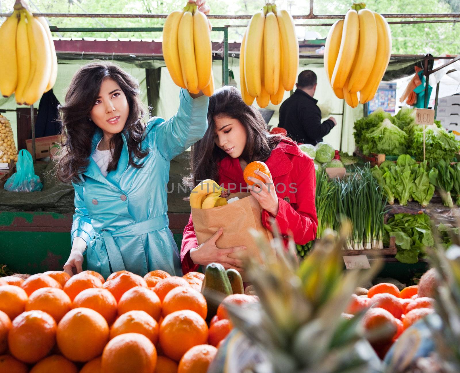 Two sister twins buying fruits at the farmers market, one holding grocery bag