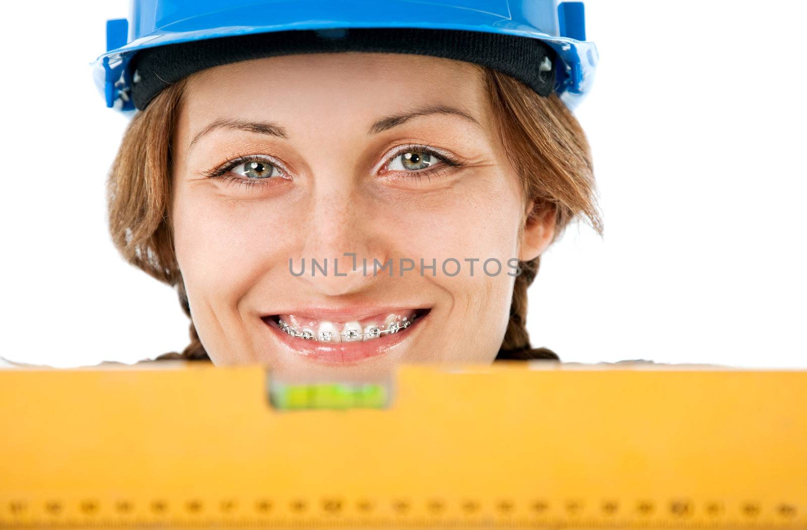 Close-up of female worker with hardhat and braces smiling behind level