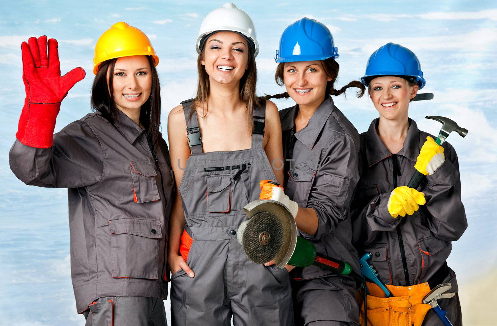Four happy female construction workers posing with instruments on beach, studio