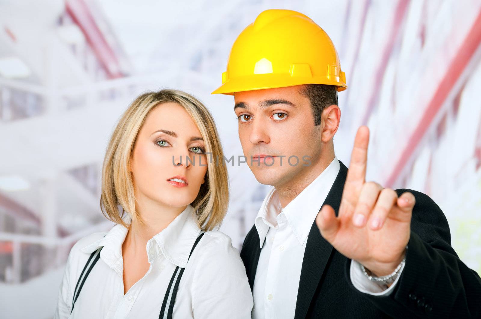 Male and female architects looking at camera, man wearing hardhat and pointing with finger