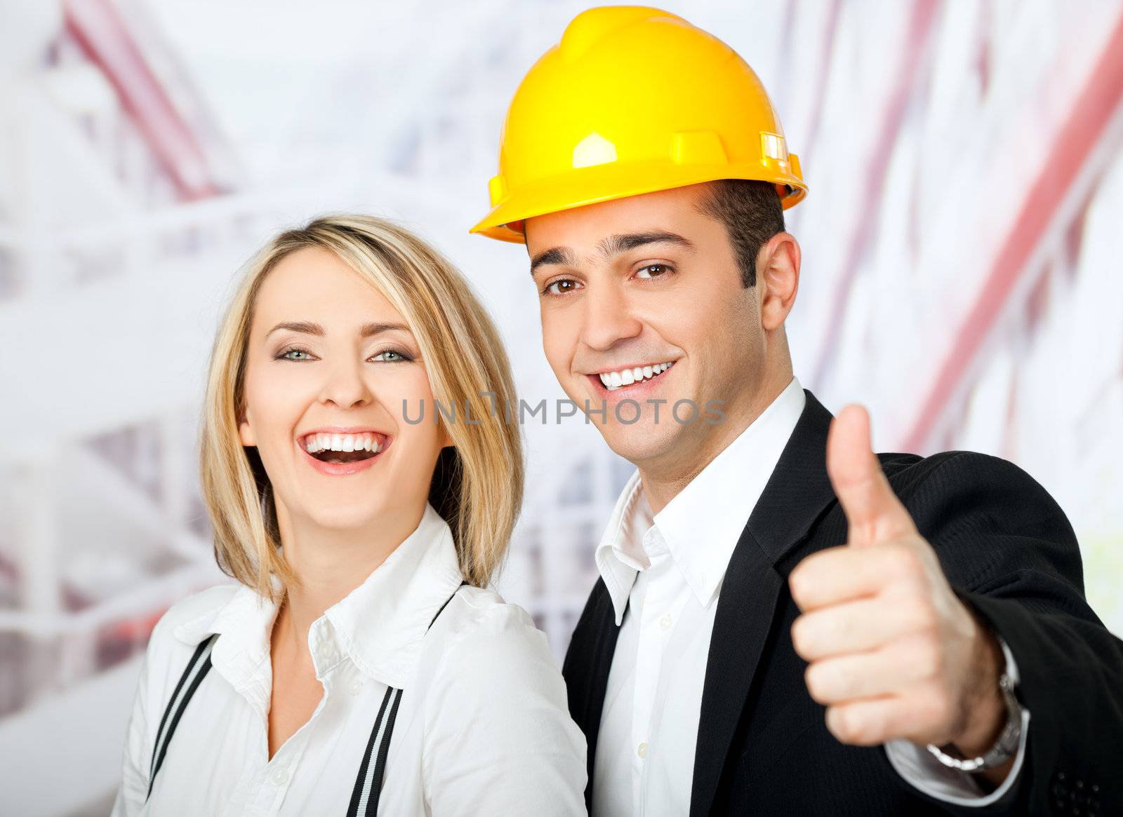 Male and female architects smiling at camera, man wearing hardhat and showing thumbs up