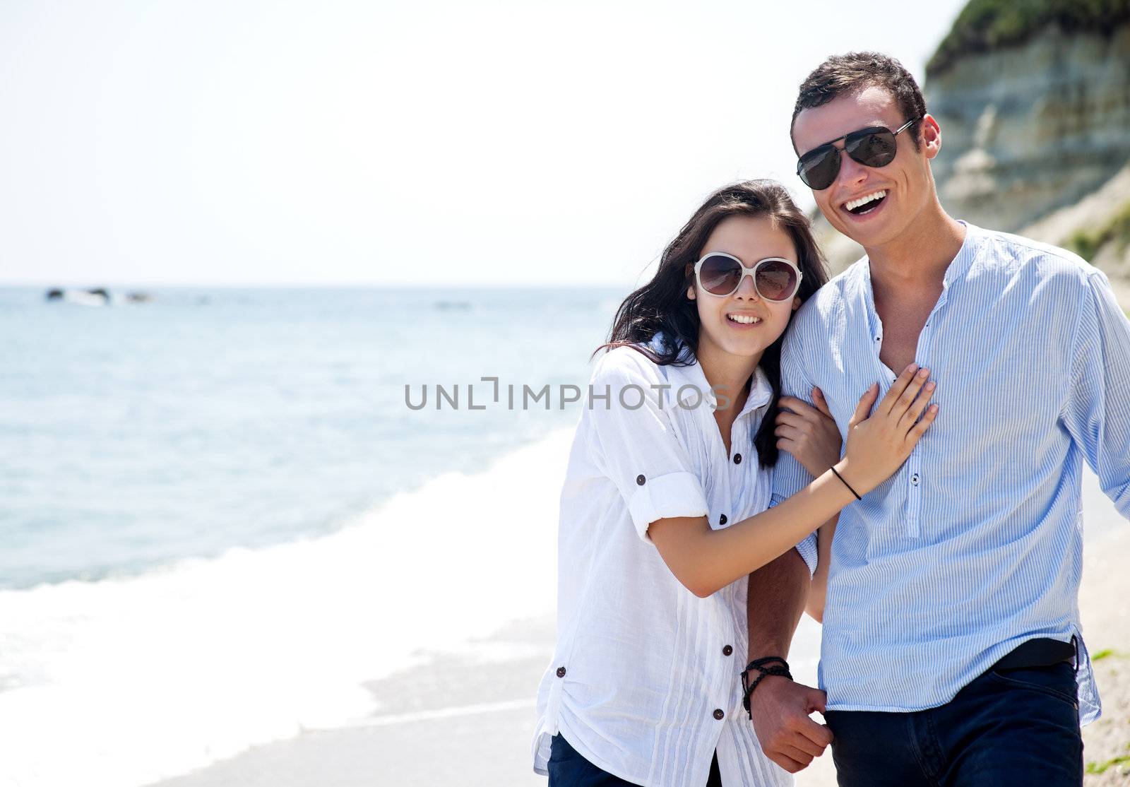 Young couple with sunglasses hugging and walking along beach