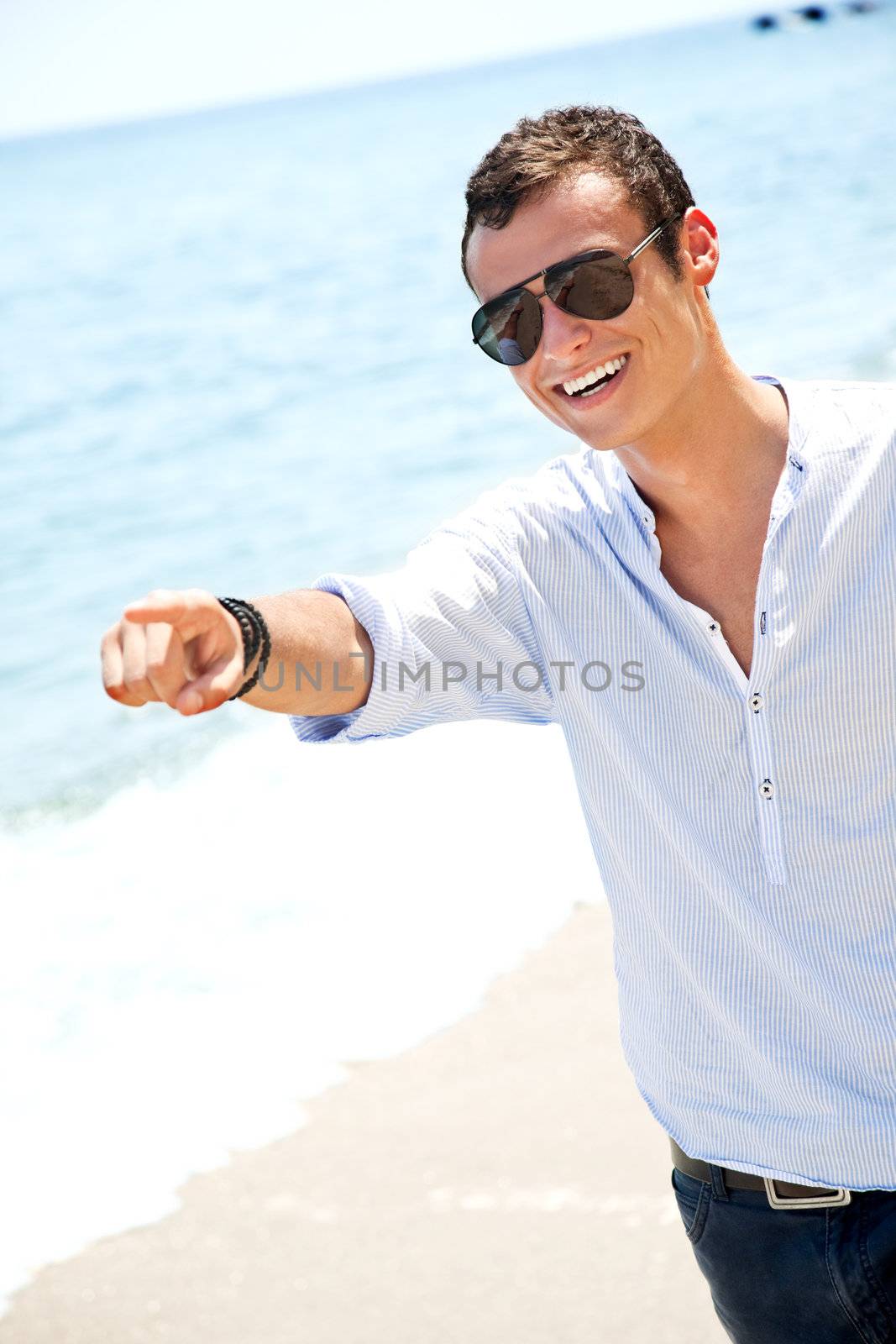 Happy handsome man with sunglasses standing on beach, pointing forward