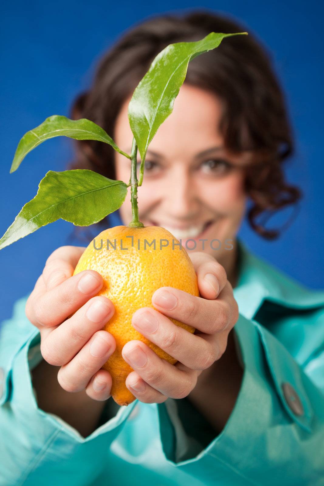Close-up of smiling female holdig fresh lemon with green leaves, focus on hands