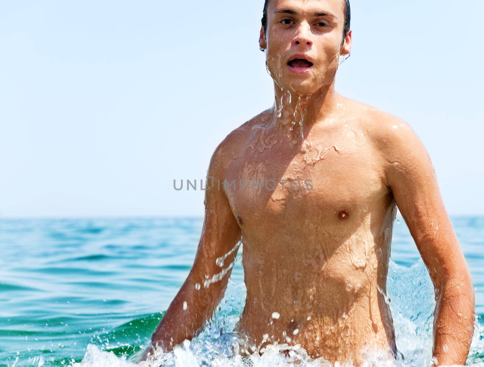 Attractive male coming out of the sea, looking at camera