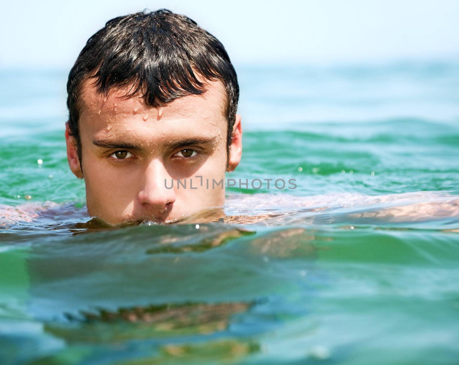 Close-up of young handsome male face in water, looking at camera