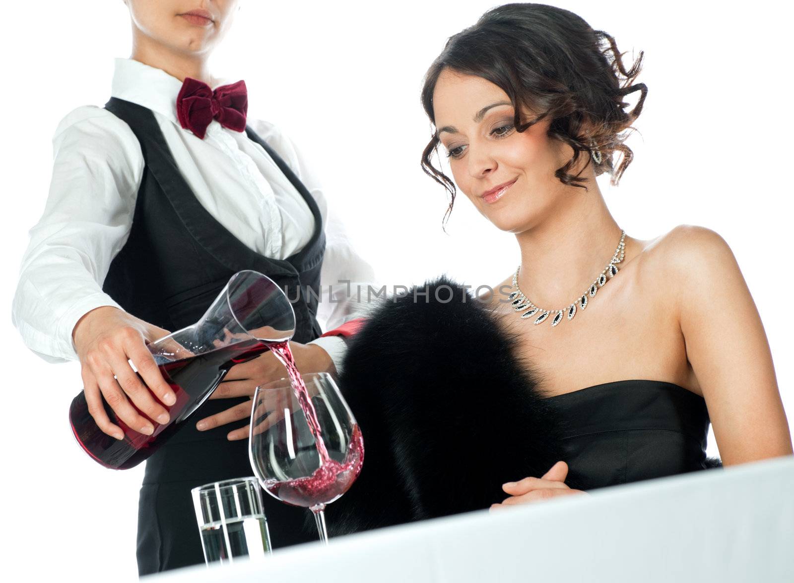 Beautiful elegant female sitting in restaurant, waitress pouring red wine, studio