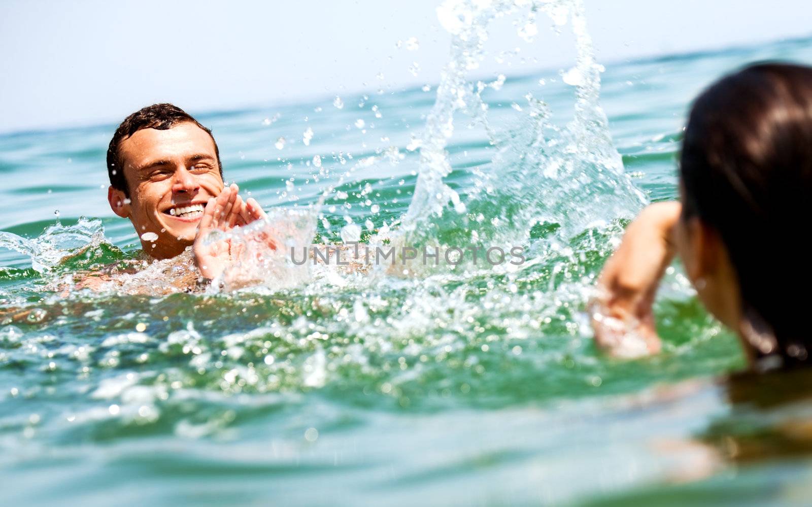 Happy couple sprinkling with water in the sea, focus on man