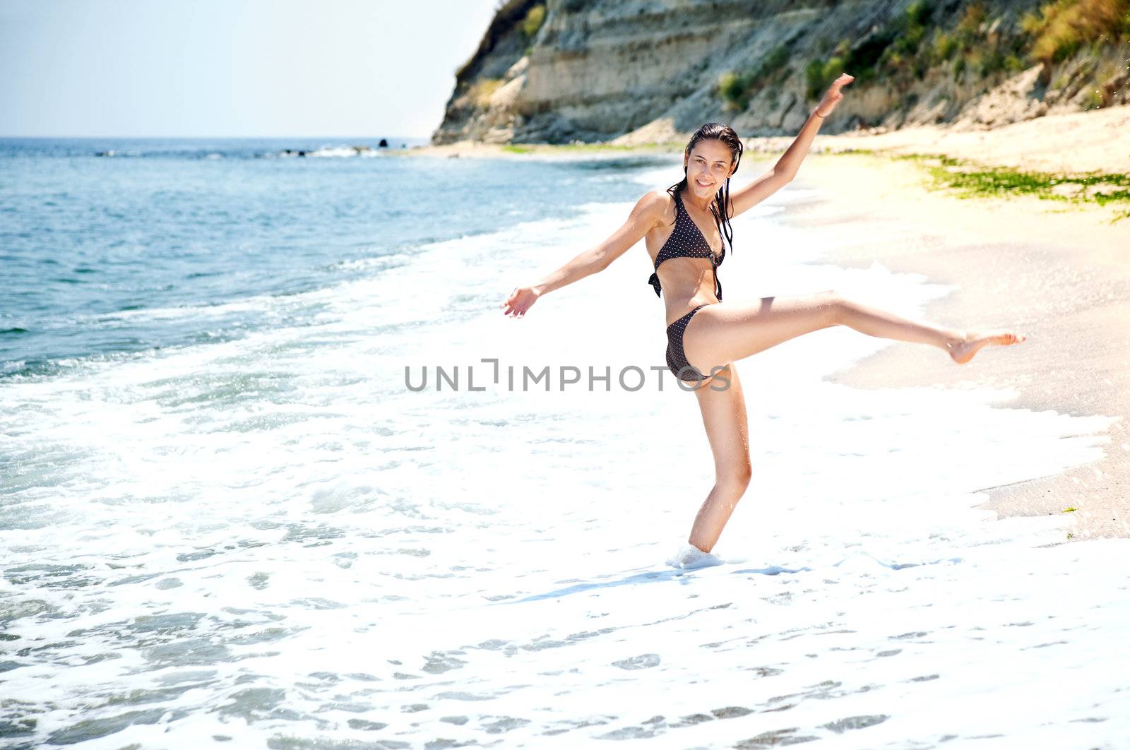 Young female enjoying water on seashore, one leg and arms raised