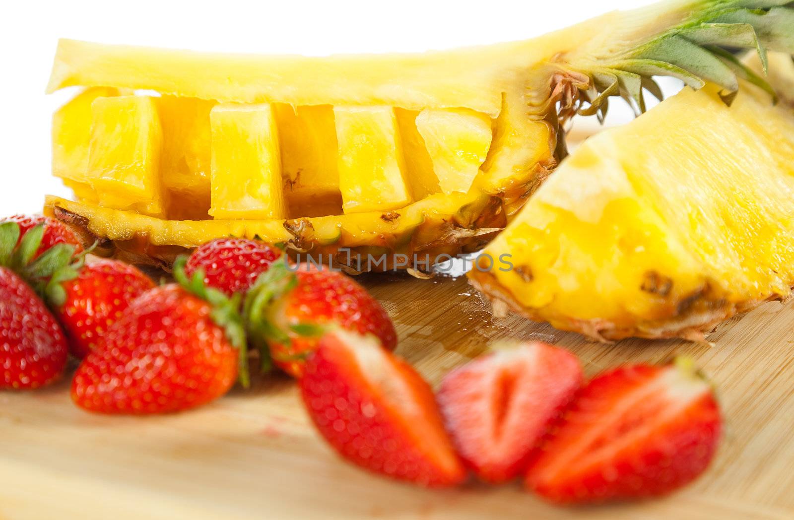 CLose-up of slices fresh strawberries and pineapple on wooden cutting board