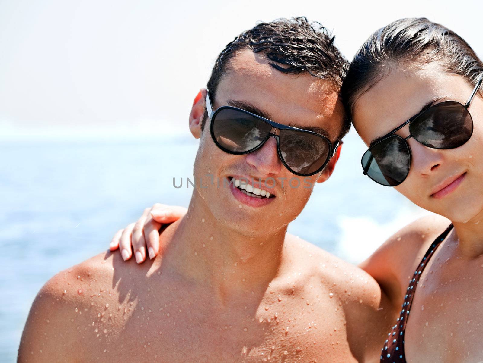young couple with sunglasses hugging and posing on beach