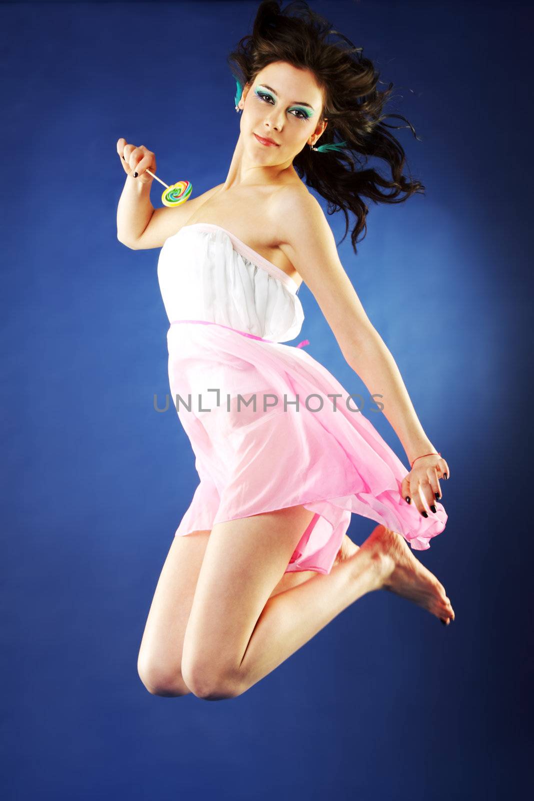 Young beautiful girl jumping in the air holding lollipop on blue