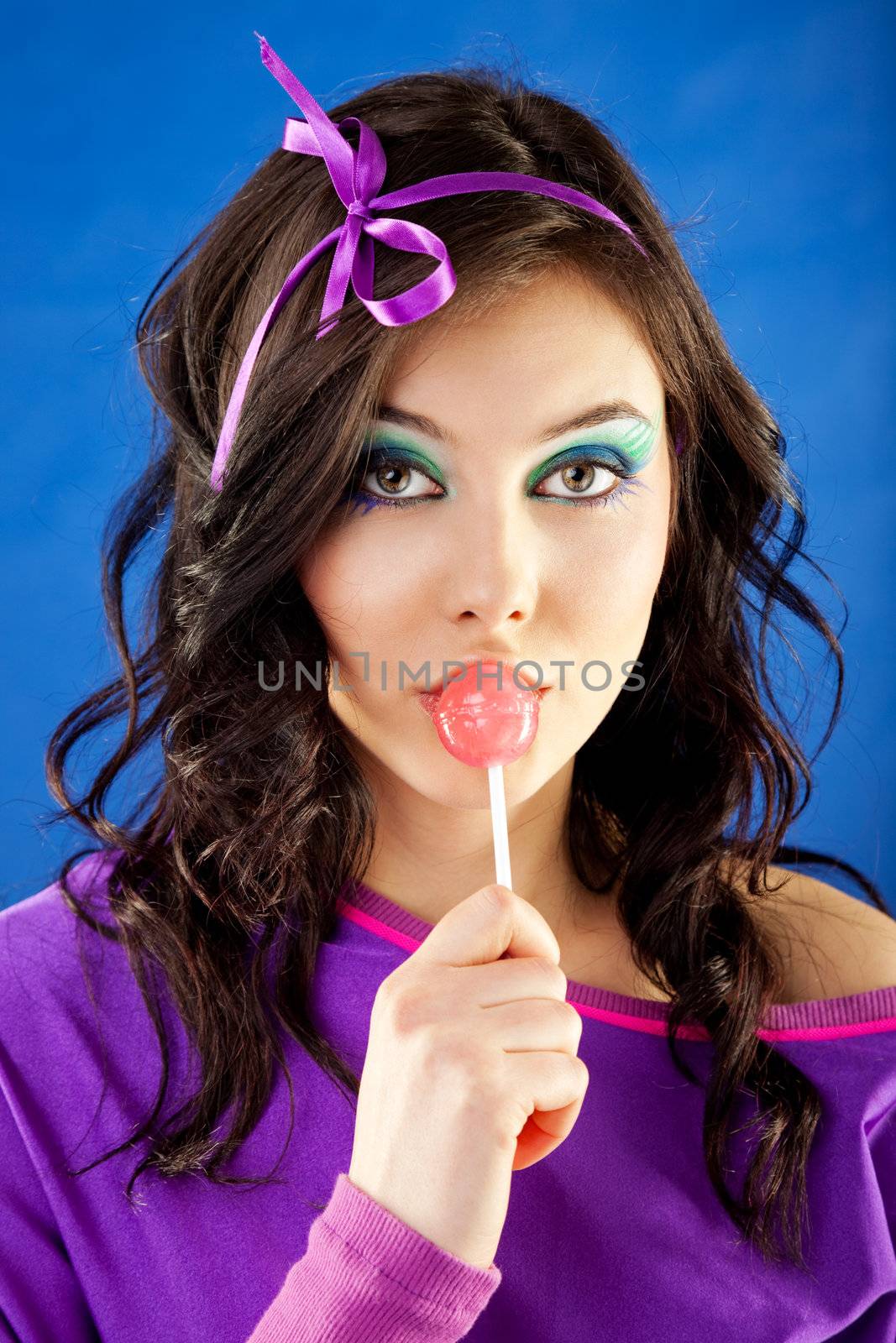 Young beautiful woman licking lollipop on blue background