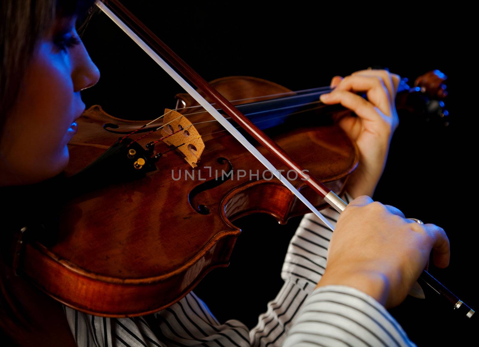 Young female violinist playing violin on black background