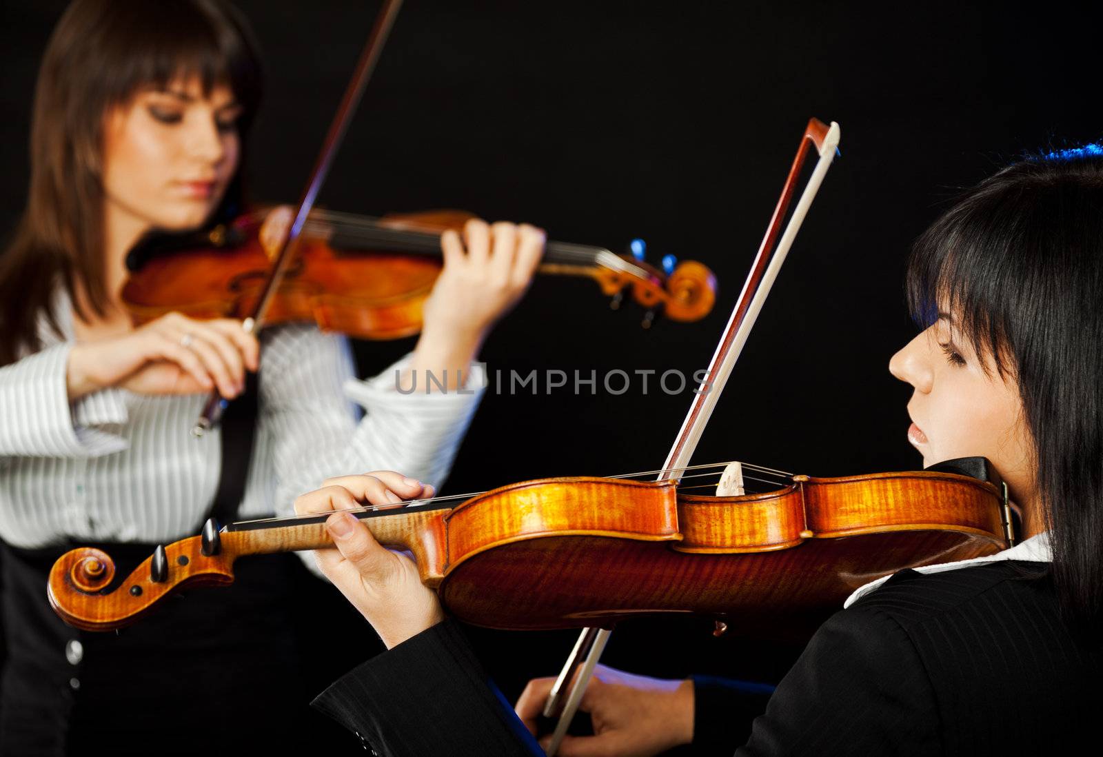 Two beautiful female violinists playing violin isolated on black