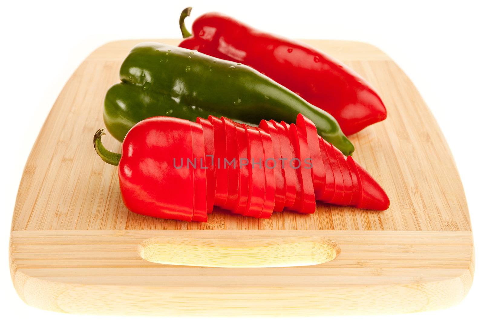 two red and a green pepper on a wooden cutting board, isolated