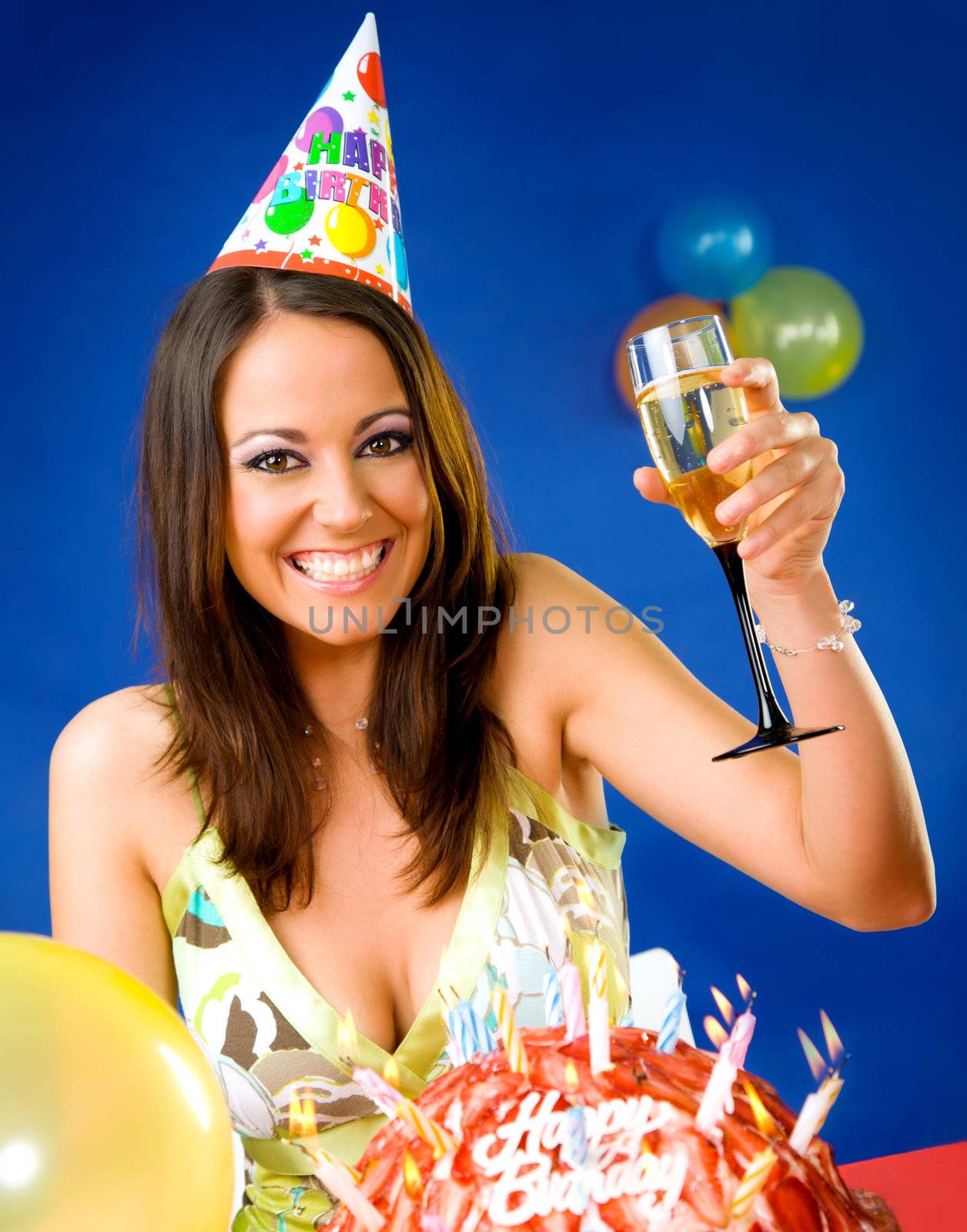 Happy female celebrating with glass of champagne and party hat over birthday cake