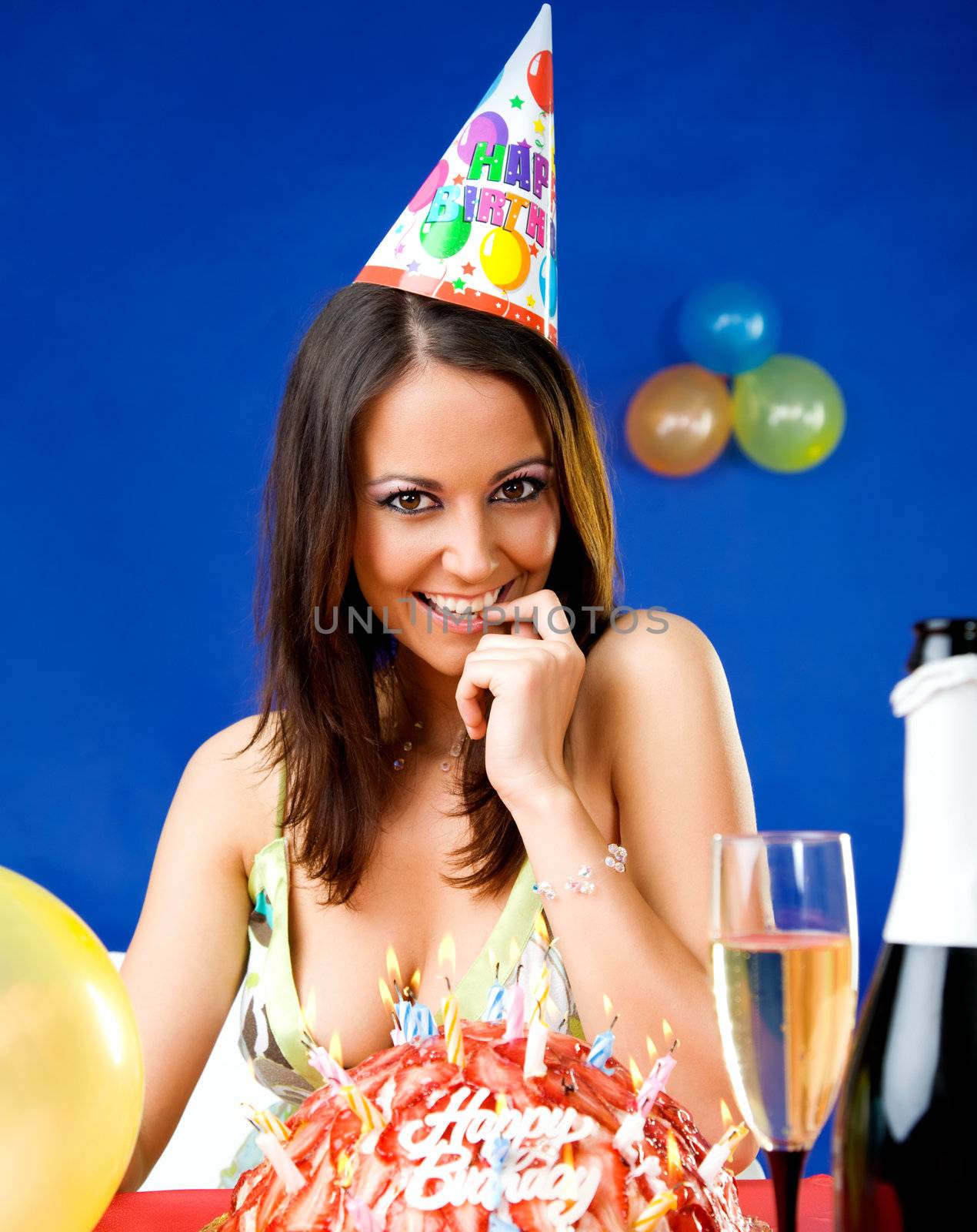 Beautiful happy female with party hat celebrating birthday over cake with candles