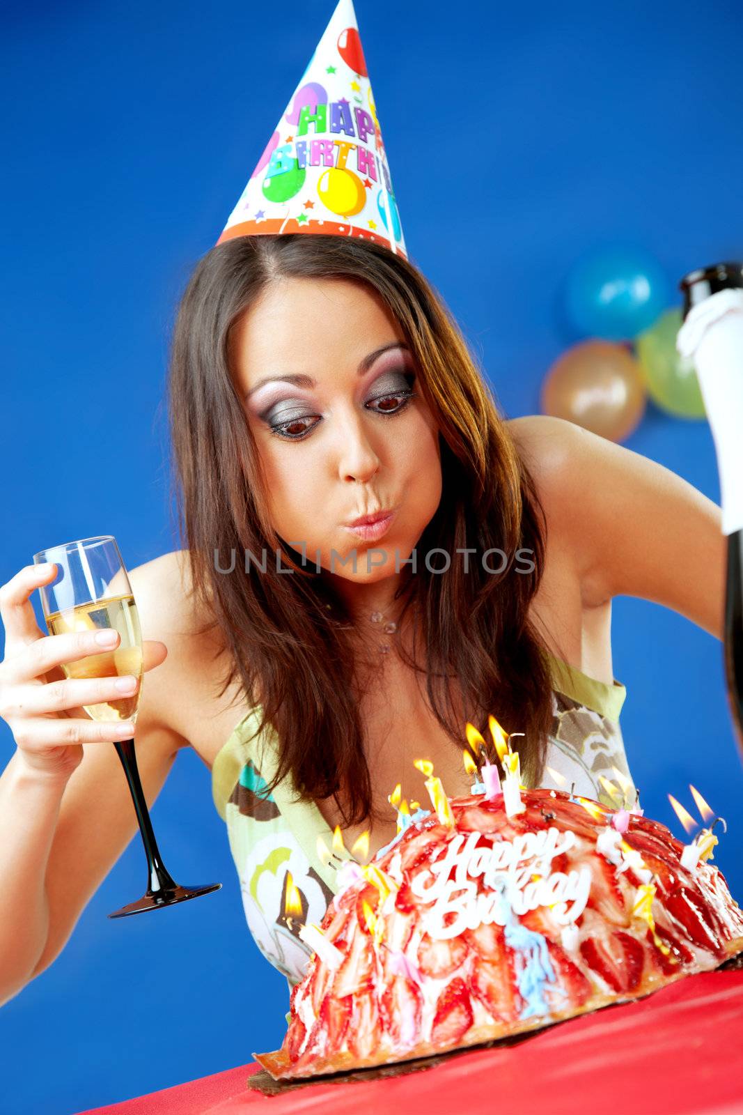 female with party hat blowing birthday cake candles, glass of wine in hand