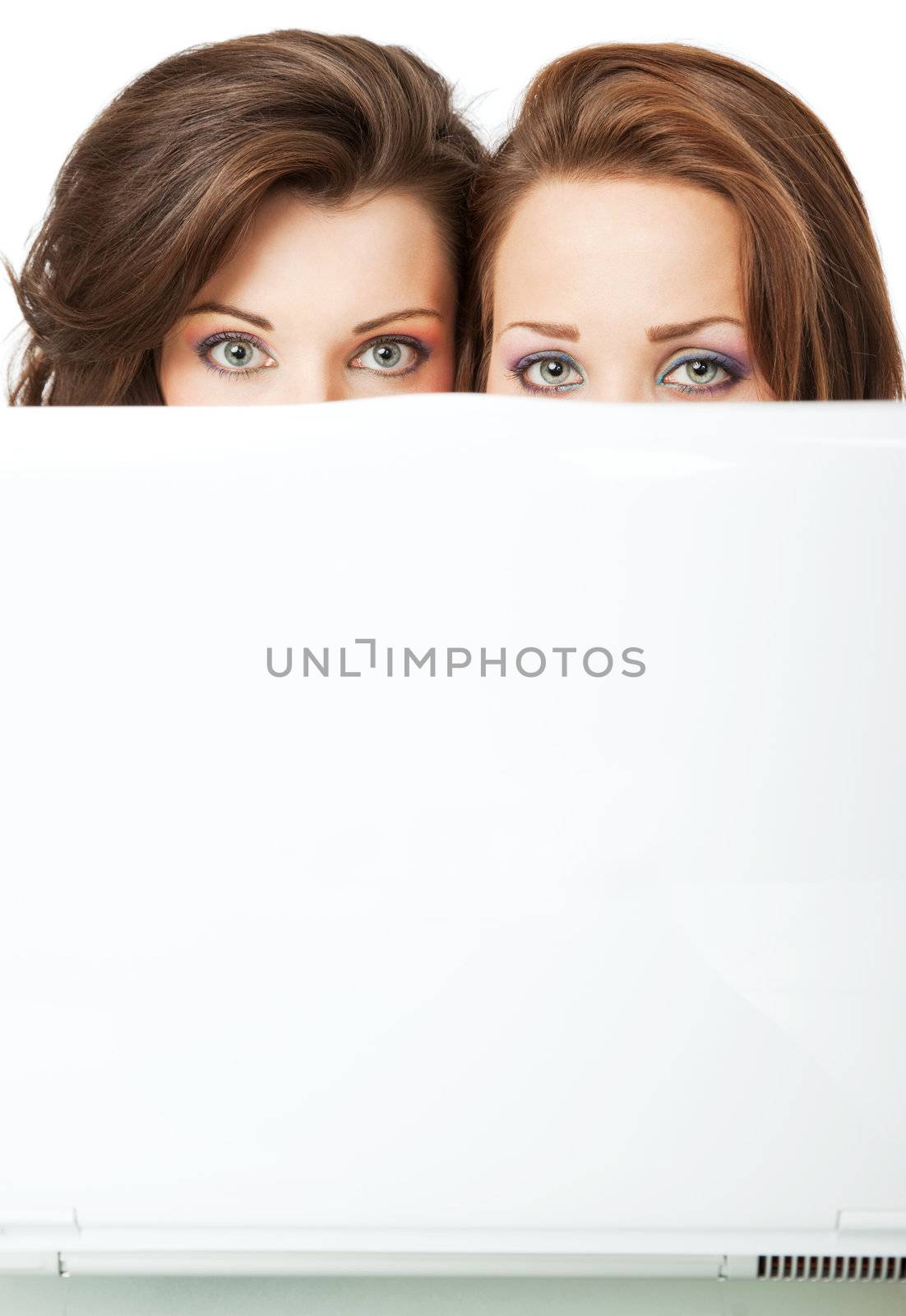 Two beautiful young females peeking behind laptop