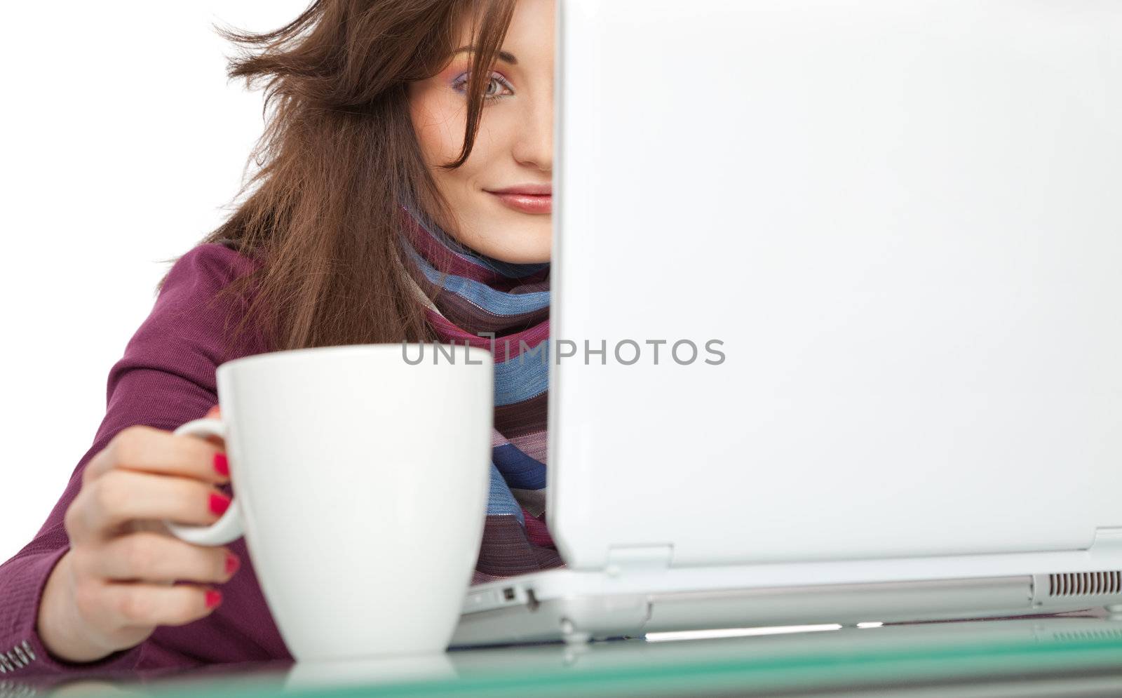 Young beautiful female sitting behind a laptop, holding a white cup