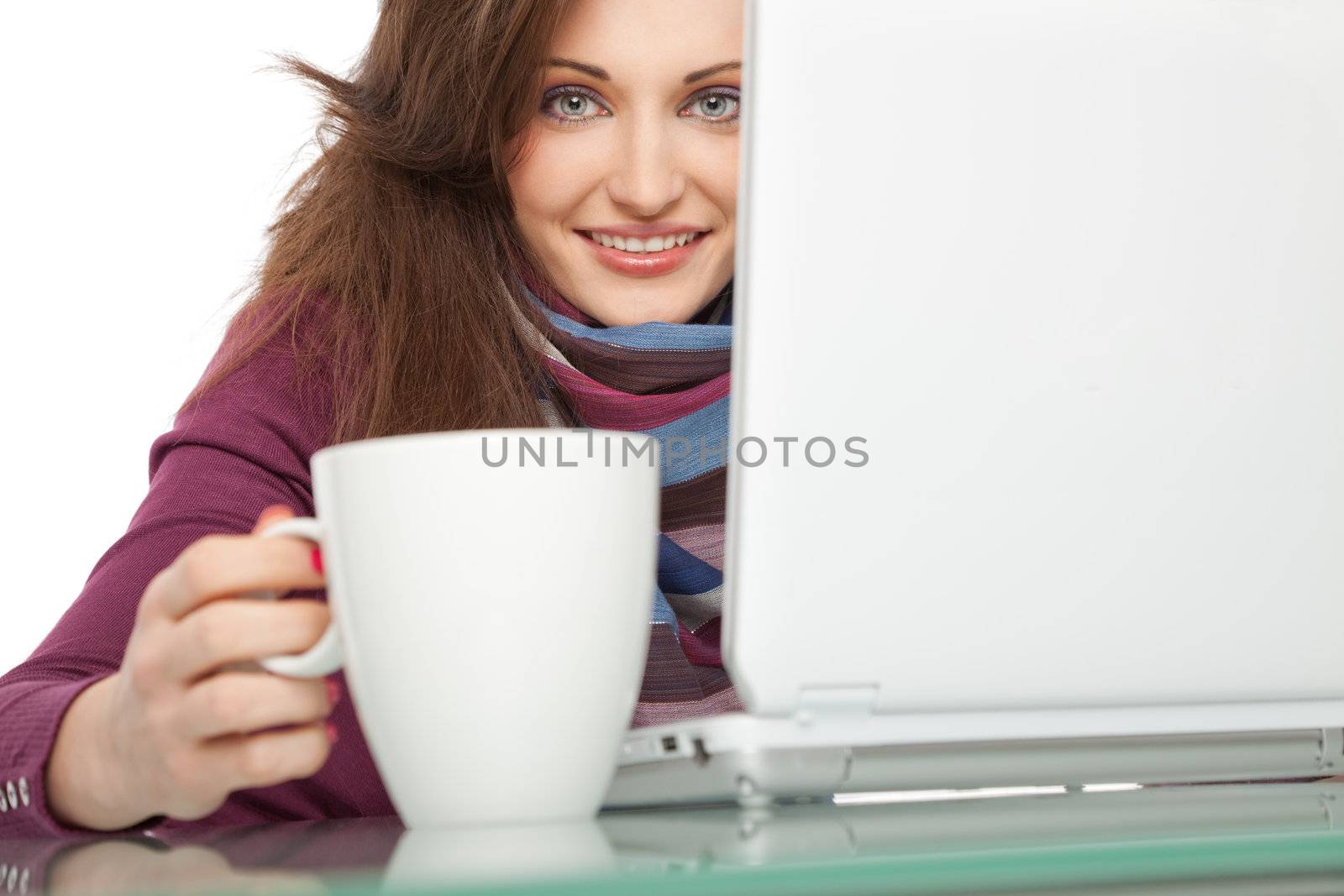 Young beautiful female behind laptop, holding a white cup, smiling at camera