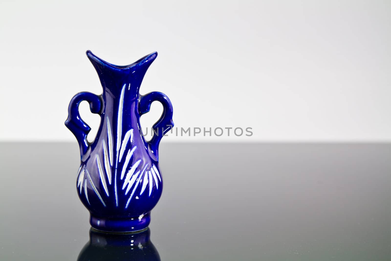 A blue empty vase on a mirror with dark and bright background