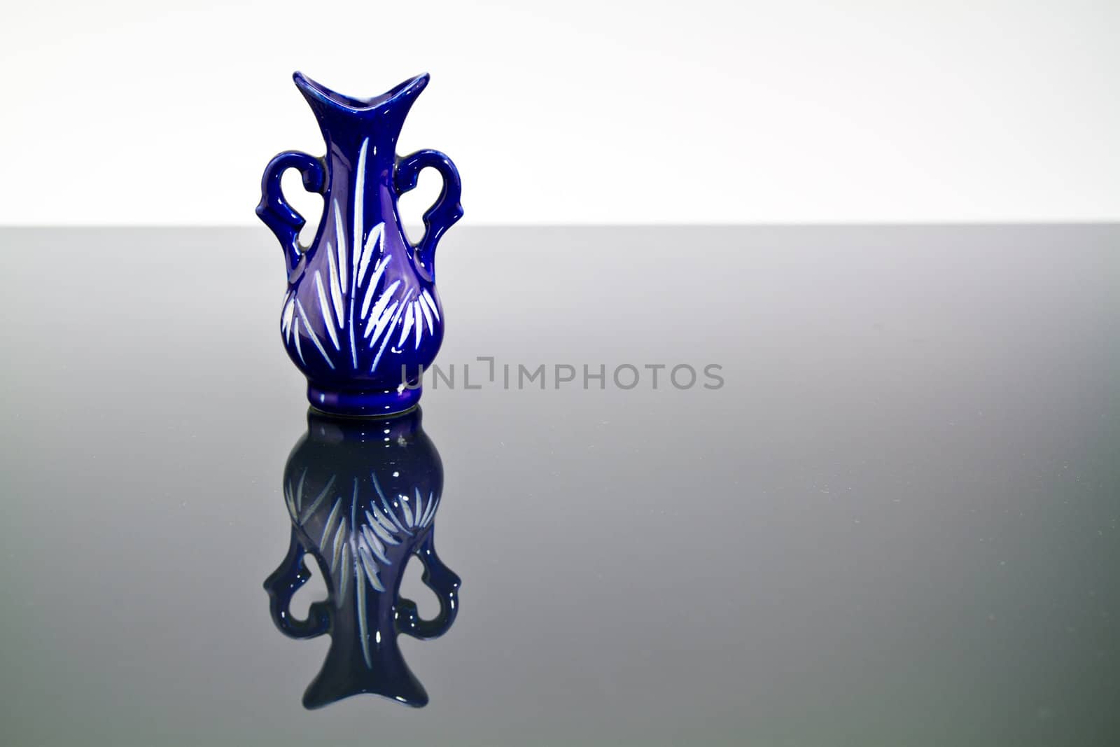 A blue empty vase on a mirror with dark and bright background and mirror image in landscape orientation