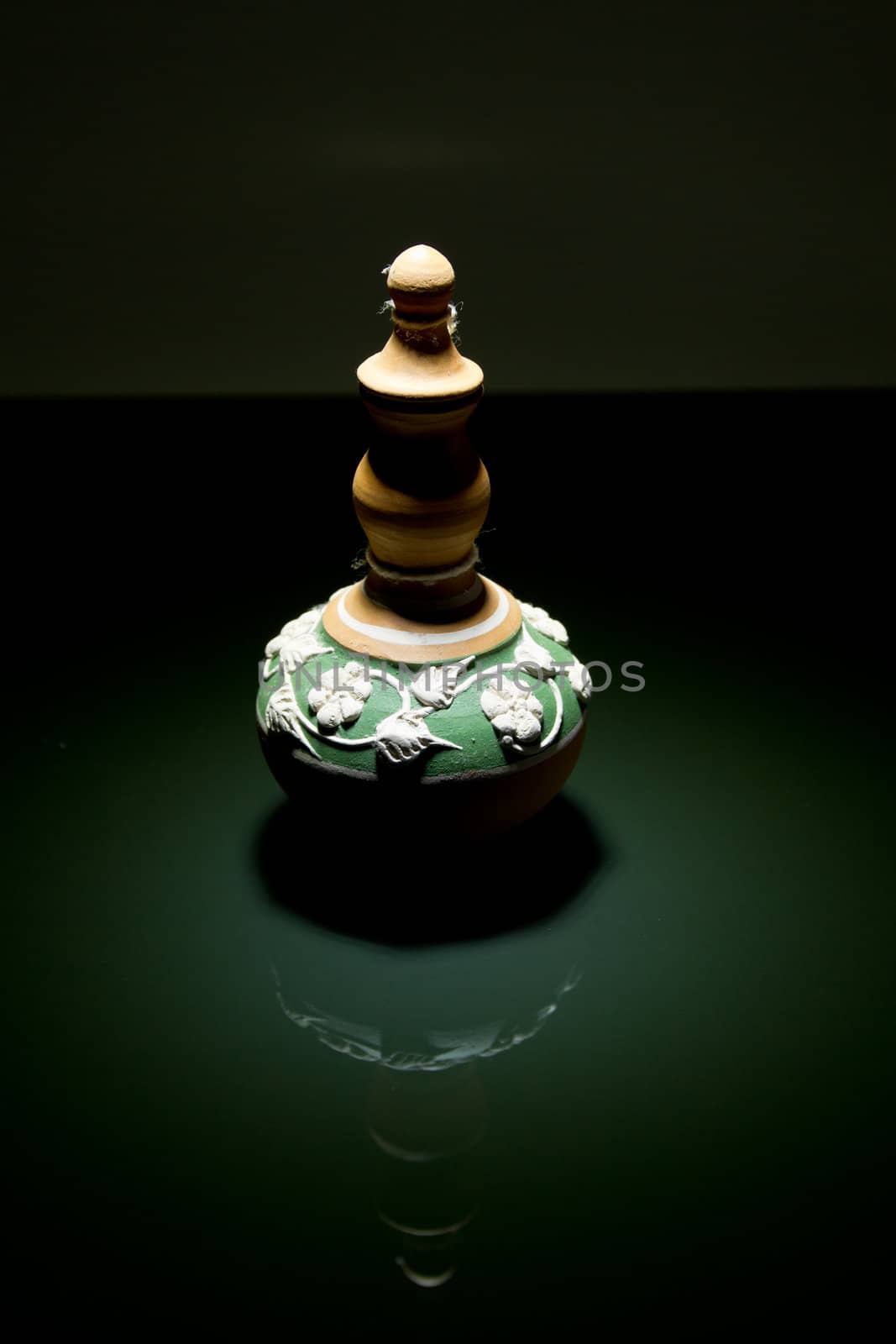 a green clay pottery on a mirror with down-lite and mirror image