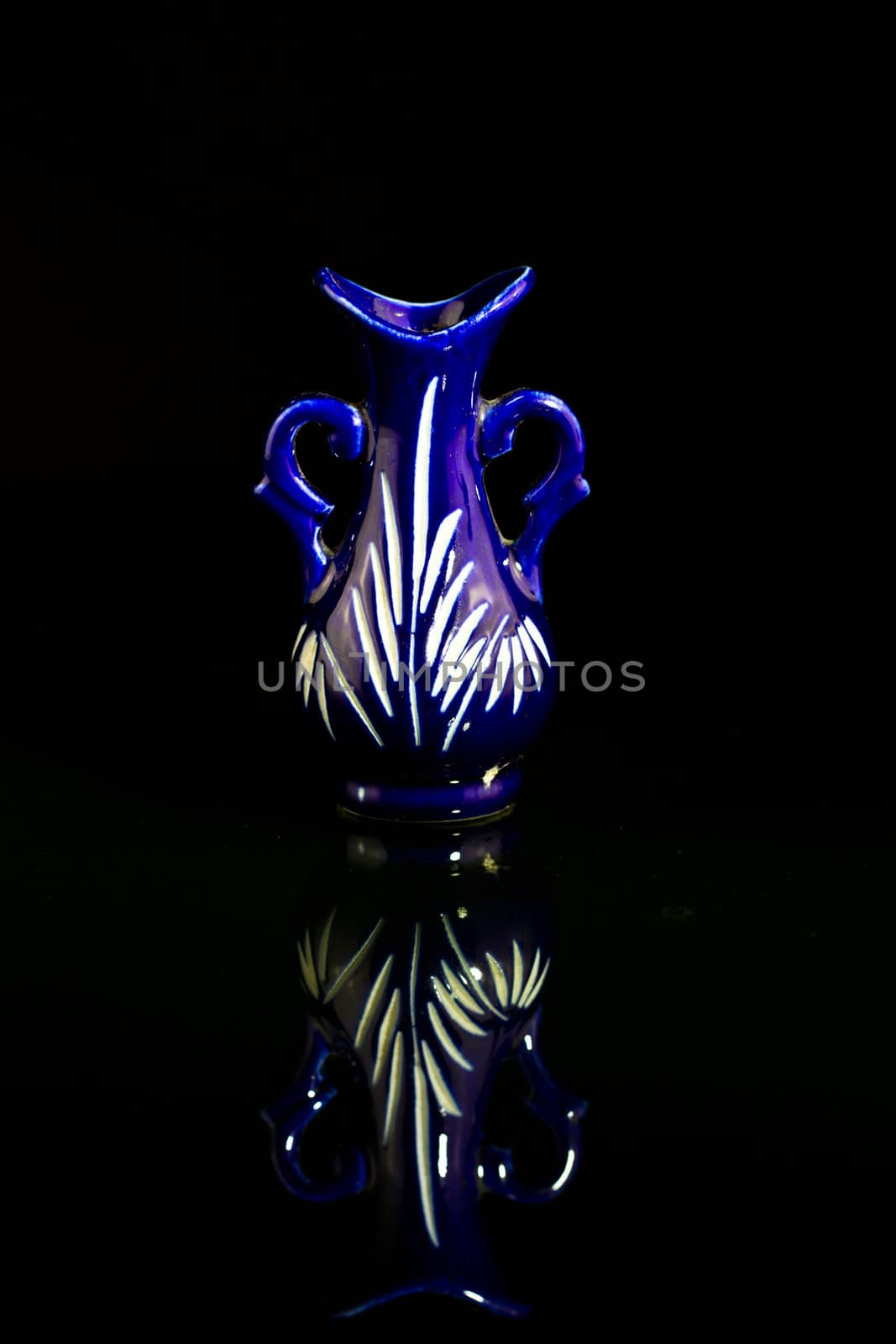 A blue empty vase on a mirror with black background and mirror image in portrait orientation