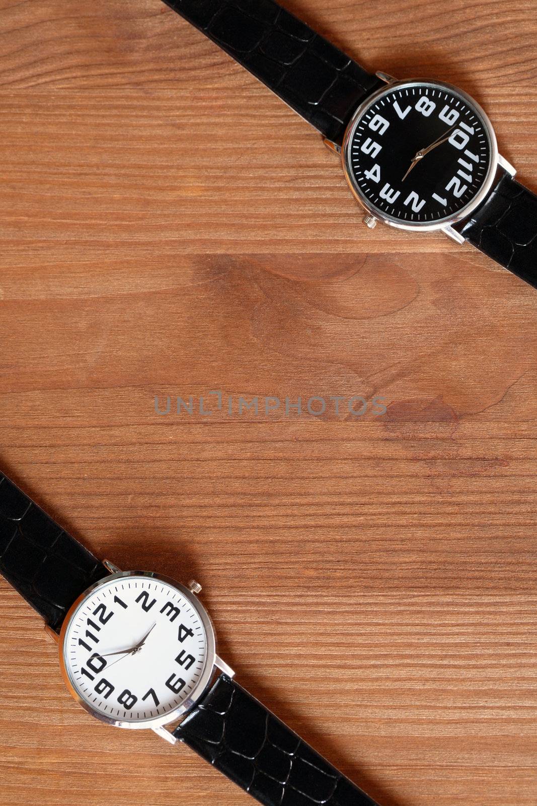 Pair of modern black and white wristwatches on wooden surface