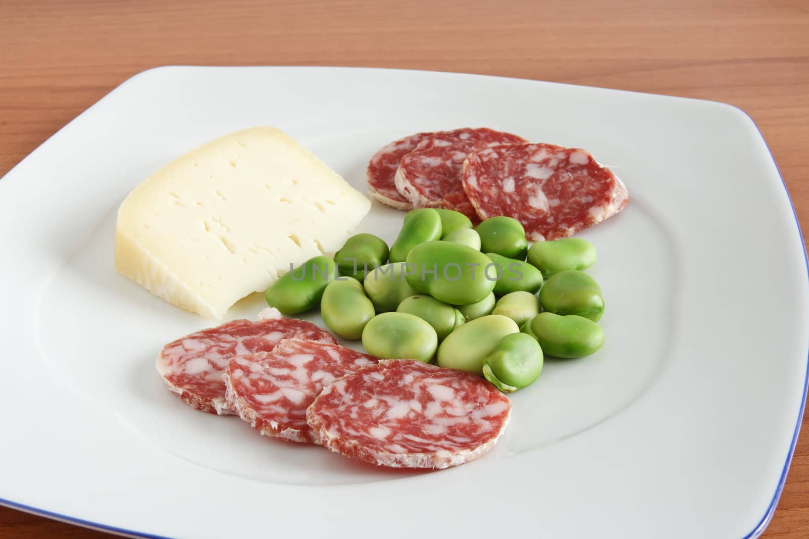 broad beans with pecorino cheese and salami slices on a white plate 
