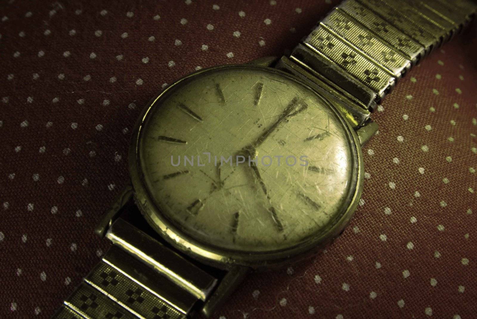 Retro golden wristwatch close up on old fashioned cloth background.