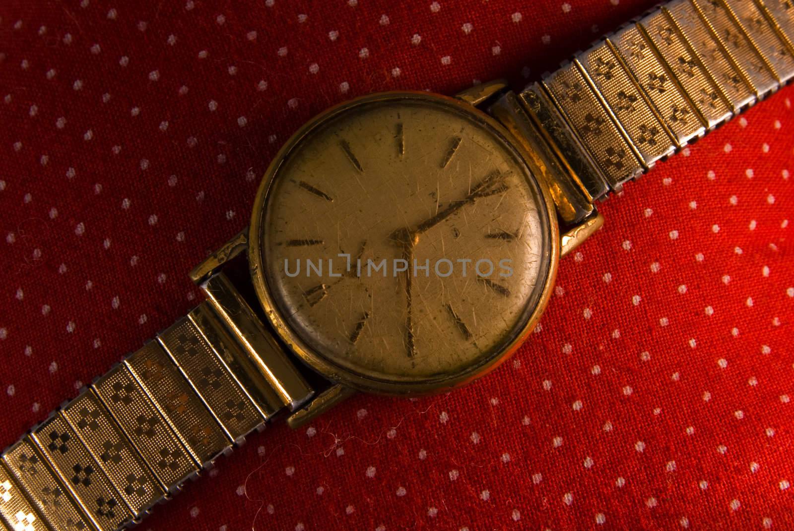 Retro golden wristwatch close up on red vintage cloth background.