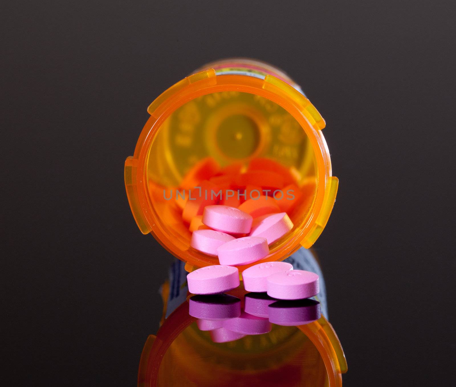 Set of round purple tablets pouring from an orange pill bottle