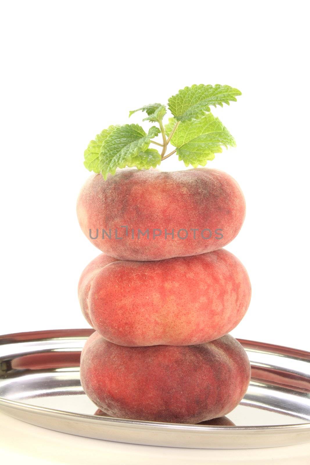 three mountain peaches on a platter with lemon balm on a white background