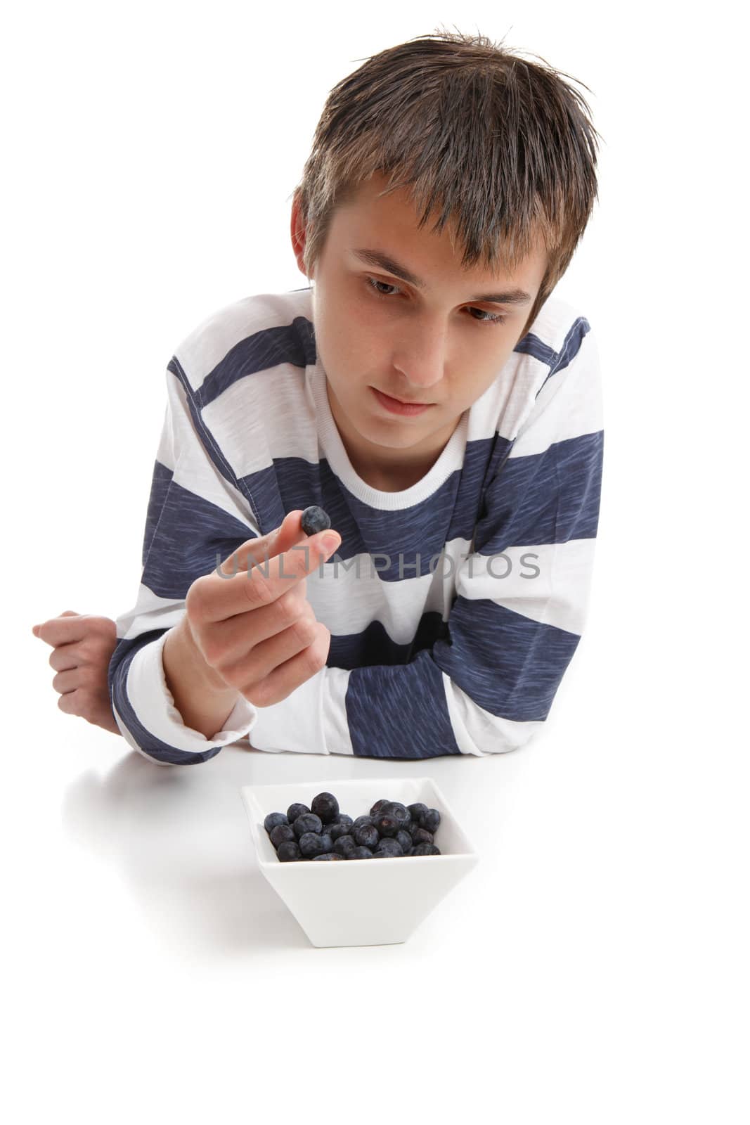 A boy looking intensely at a blueberry held between two fingers.