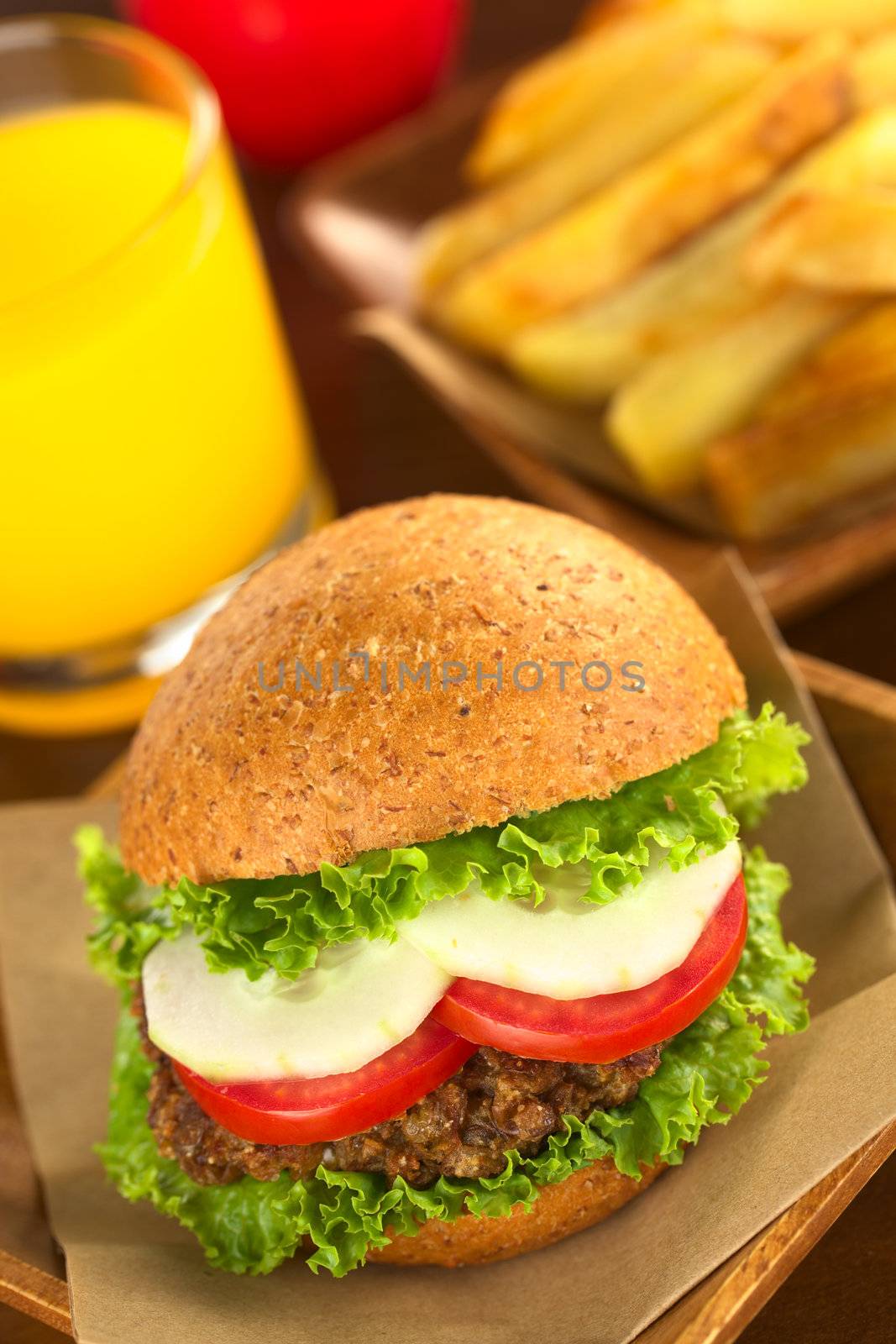 Vegetarian lentil burger in wholewheat bun with lettuce, tomato and cucumber accompanied by French fries and orange juice (Selective Focus, Focus on the front of the sandwich) 