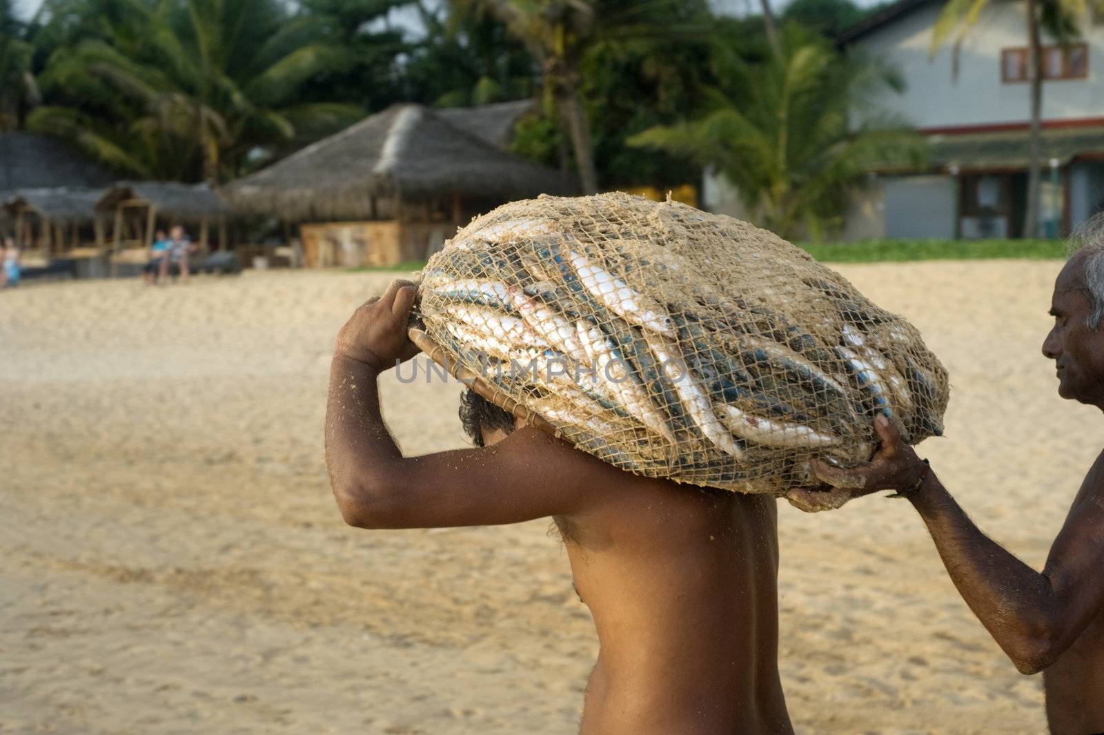 Hikkaduwa, Sri Lanka - February 21, 2011: Two Sri Lankan fishermen carrying  sack with fish to their home. Fishing in Sri Lanka is a tough job but this is the way they earn their living