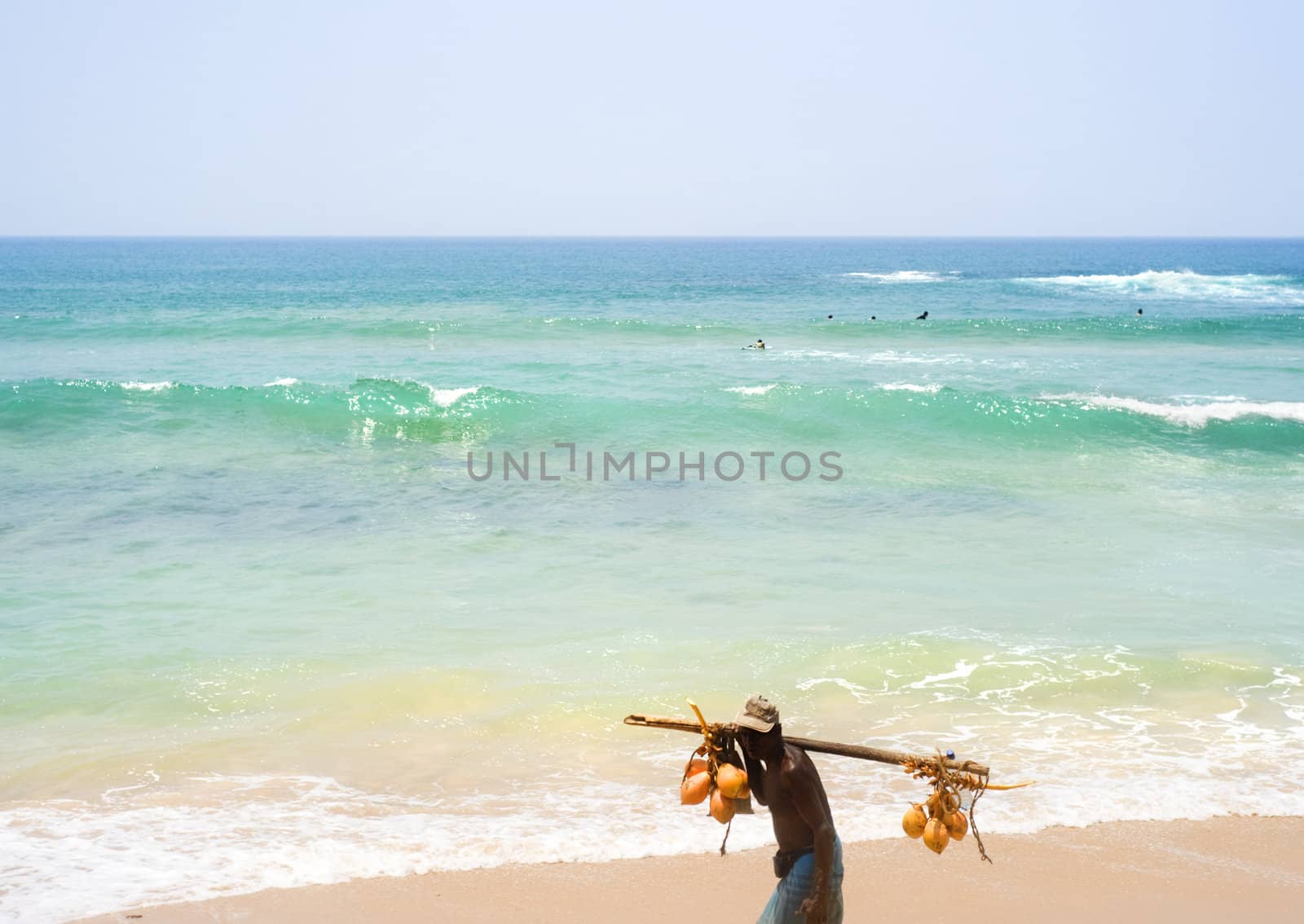 Hikkaduwa, Sri Lanka - March 11, 2011: Local Sri Lankan trader walking along the beach with a coconut on his shoulders try to selling it