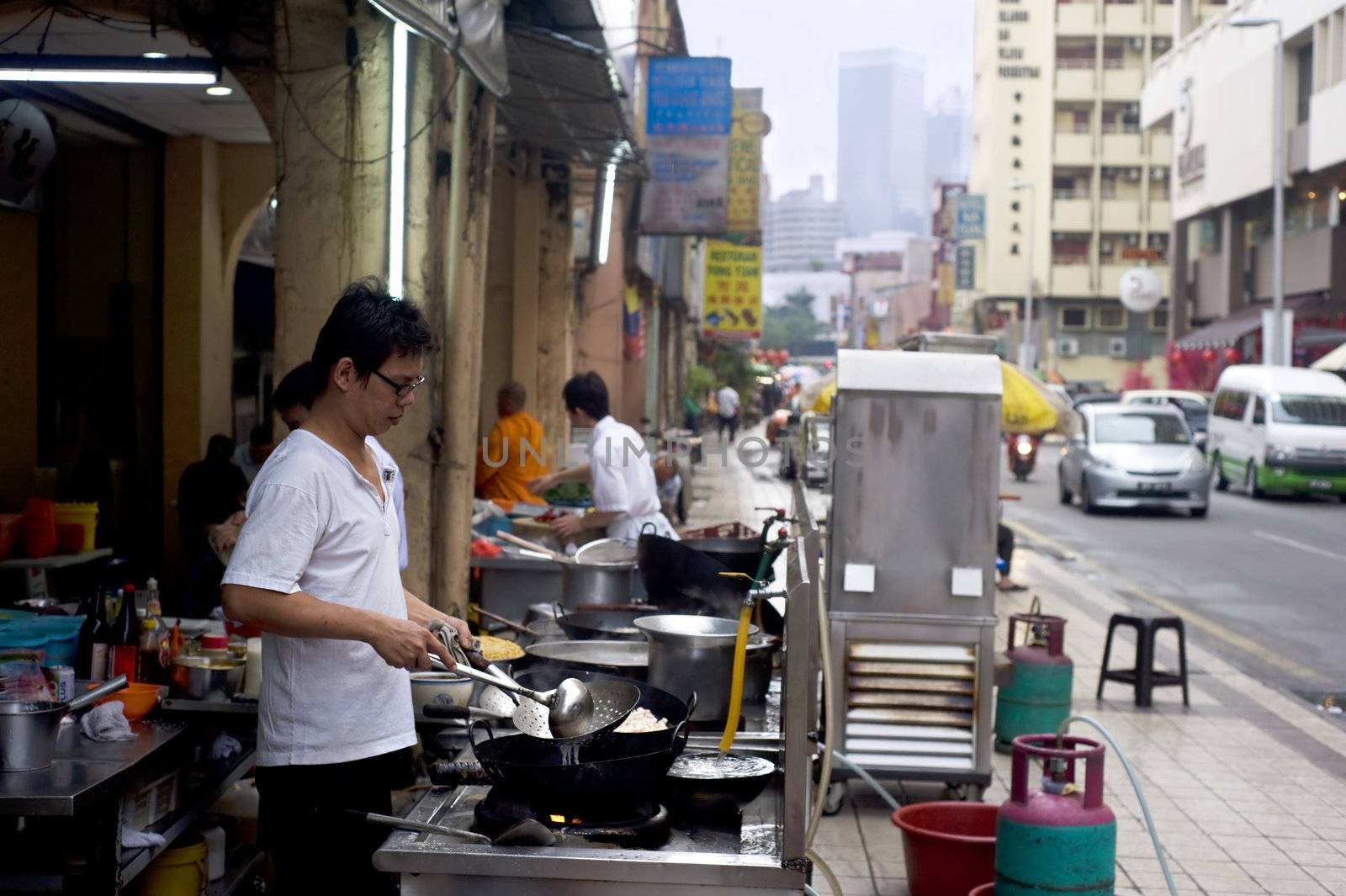 Kuala Lumpur, Malaysia - March 17, 2011: Local man cooking fast food on the street in Kuala Lumpur's Chinatown. KL Chinatown is a popular tourist attraction and a food haven