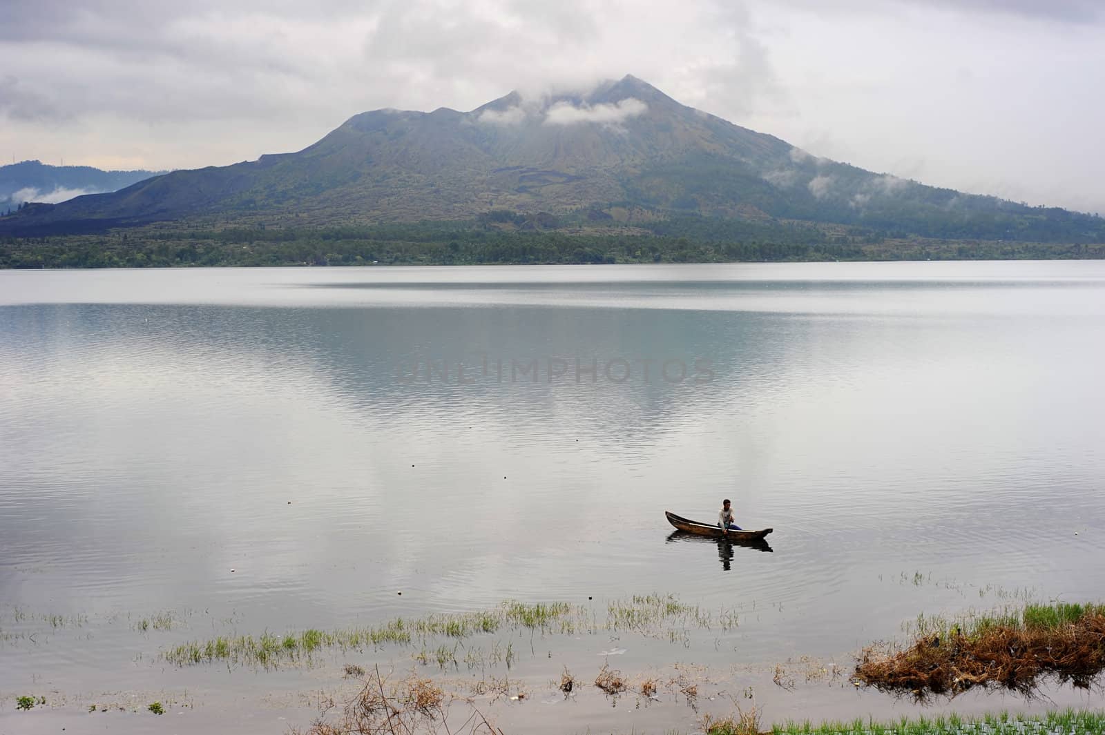 Bali island,Indonesia - April 10,2011: Man fishing in a caldera lake of Batur volcano. Batur is the most active volcano on the popular tourist island of Bali and one of Inondesia's more active ones on Bali