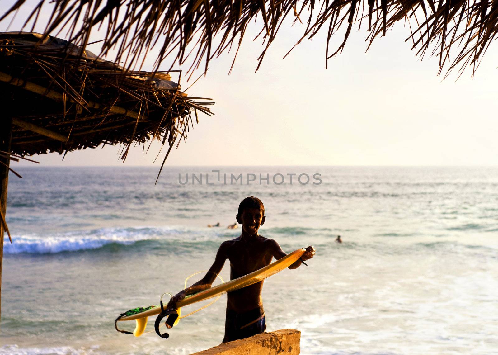 Hikkaduwa, Sri Lanka - January 23, 2011: Portrait of young local surfer with surfboard in front of the ocean
