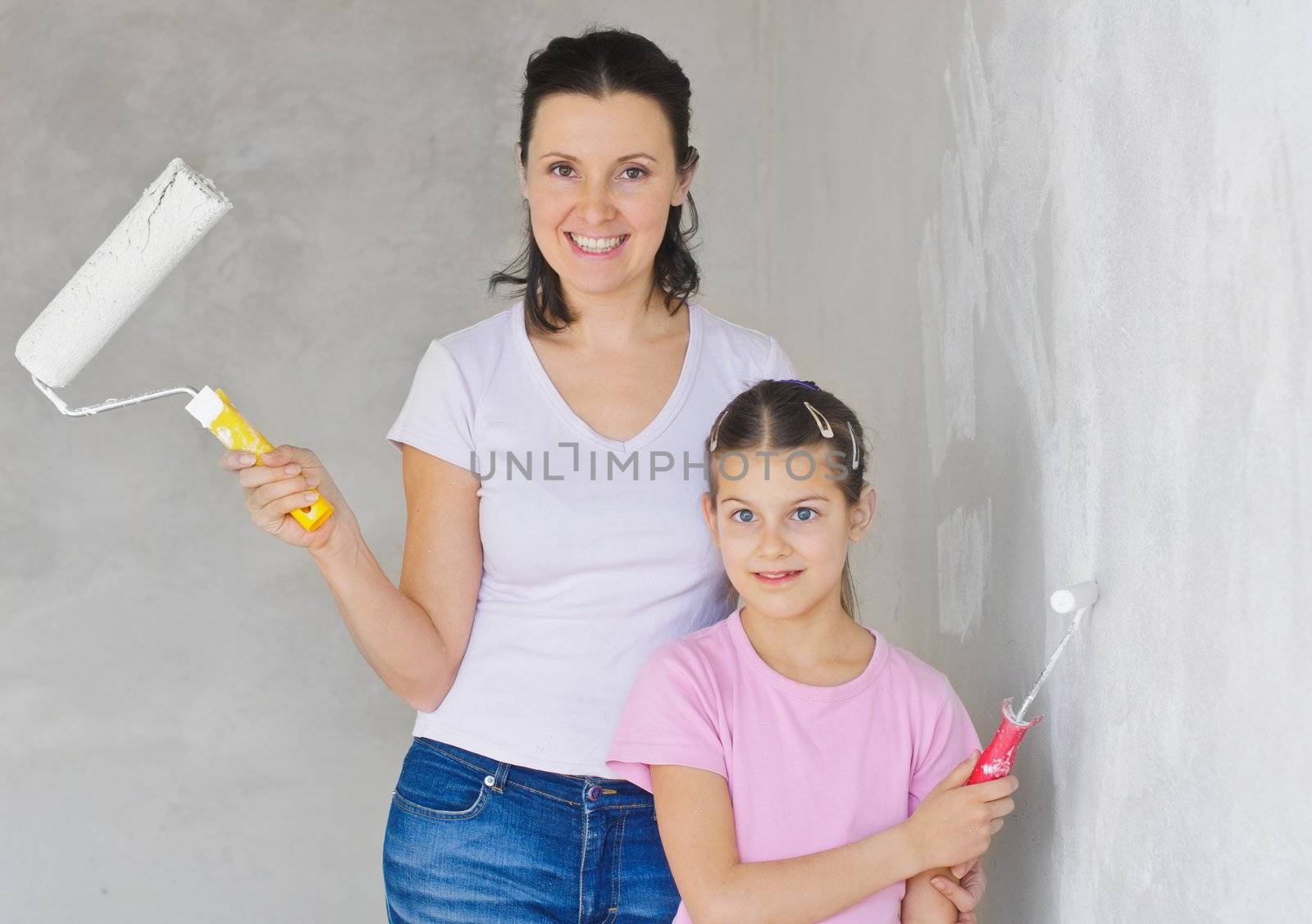 Happy Mother and douther painting a wall with roller